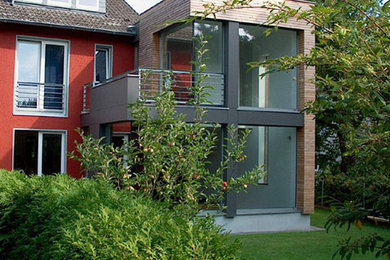 Small and brown contemporary two floor terraced house in Cologne with wood cladding and a flat roof.
