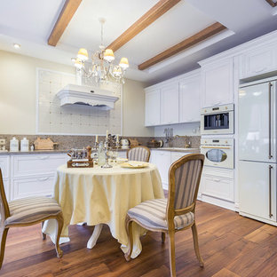 Свежая идея для дизайна: угловая кухня в классическом стиле с белыми фасадами, столешницей из акрилового камня, белой техникой, паркетным полом среднего тона, накладной раковиной, фасадами с утопленной филенкой и бежевым фартуком без острова - отличное фото интерьера