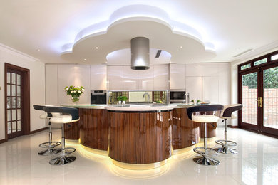 Expansive contemporary u-shaped eat-in kitchen in London with flat-panel cabinets, medium wood cabinets, solid surface benchtops, metallic splashback, glass sheet splashback, stainless steel appliances, porcelain floors and with island.