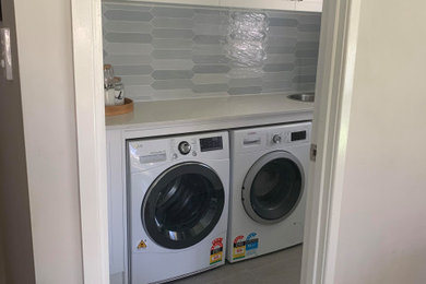 Photo of a small modern single-wall dedicated laundry room in Sydney with a drop-in sink, shaker cabinets, white cabinets, quartz benchtops, blue splashback, porcelain splashback, white walls, porcelain floors, a side-by-side washer and dryer, grey floor and white benchtop.