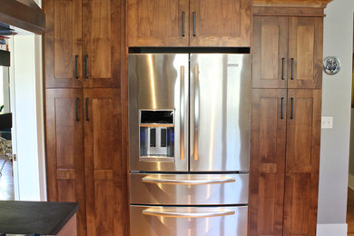 Mid-sized arts and crafts l-shaped medium tone wood floor open concept kitchen photo in Seattle with a farmhouse sink, shaker cabinets, medium tone wood cabinets, solid surface countertops, black backsplash and stainless steel appliances