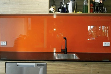Modern inredning av en hemmabar, med orange stänkskydd och glaspanel som stänkskydd