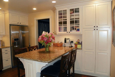 Mid-sized elegant l-shaped medium tone wood floor enclosed kitchen photo in Other with an undermount sink, raised-panel cabinets, white cabinets, granite countertops, white backsplash, porcelain backsplash, stainless steel appliances and a peninsula