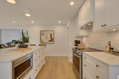 Inspiration for a transitional l-shaped vinyl floor and brown floor eat-in kitchen remodel in Edmonton with a single-bowl sink, shaker cabinets, white cabinets, quartz countertops, white backsplash, porcelain backsplash, stainless steel appliances, an island and white countertops