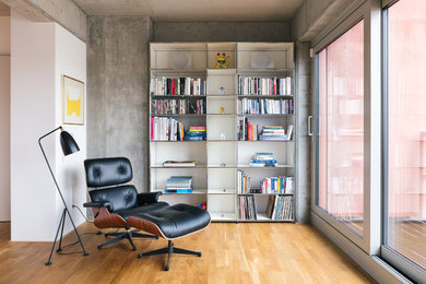 Industrial living room in Berlin with a library, grey walls and medium hardwood floors.
