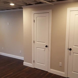 Diseño de sótano con ventanas tradicional renovado, de tamaño medio, con paredes beige, suelo de madera oscura, chimenea lineal, marco de chimenea de yeso y suelo marrón