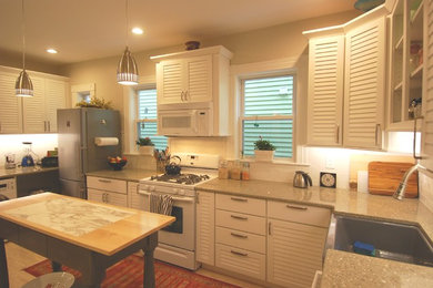 Mid-sized trendy l-shaped light wood floor and beige floor open concept kitchen photo in Boston with a farmhouse sink, louvered cabinets, white cabinets, recycled glass countertops, white backsplash, subway tile backsplash, white appliances and an island