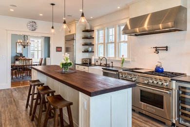 Photo of a beach style separate kitchen in Boston with a farmhouse sink, white cabinets, wood benchtops, white splashback, stainless steel appliances, dark hardwood floors and with island.