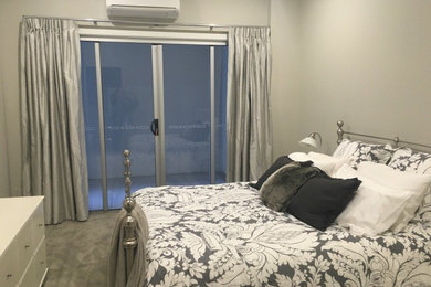 This is an example of a medium sized contemporary bedroom in Brisbane with white walls, carpet, no fireplace and grey floors.