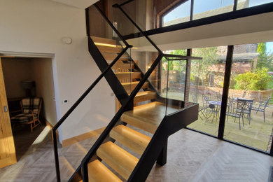 Modern wood l-shaped metal railing staircase in Other with open risers and feature lighting.