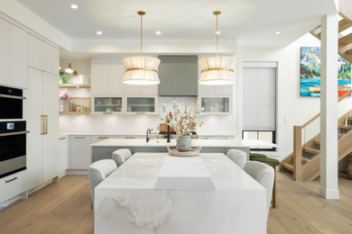 Example of a trendy l-shaped light wood floor and beige floor open concept kitchen design in Other with an undermount sink, flat-panel cabinets, white cabinets, white backsplash, stainless steel appliances, an island and white countertops