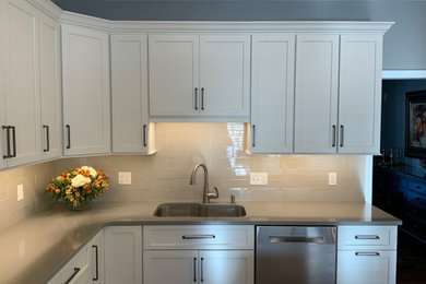 Example of a large classic l-shaped medium tone wood floor and brown floor kitchen pantry design in Boston with an undermount sink, shaker cabinets, white cabinets, quartz countertops, gray backsplash, ceramic backsplash, stainless steel appliances, an island and gray countertops