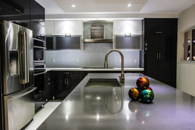 This is an example of a large modern l-shaped open plan kitchen in Miami with a drop-in sink, flat-panel cabinets, black cabinets, quartz benchtops, metallic splashback, glass tile splashback, stainless steel appliances, porcelain floors, with island, white floor and grey benchtop.
