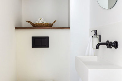 This is an example of a small contemporary cloakroom in London with white cabinets, a wall mounted toilet, white tiles, stone slabs, white walls, pebble tile flooring, a wall-mounted sink, multi-coloured floors and a floating vanity unit.