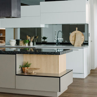 Contemporary kitchen pantry inspiration - Example of a trendy l-shaped dark wood floor kitchen pantry design in Adelaide with an undermount sink, flat-panel cabinets, white cabinets, granite countertops, black backsplash, mirror backsplash, stainless steel appliances and an island