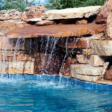 Free form pool with stone table, sun shelf, water feature, and outdoor kitchen,