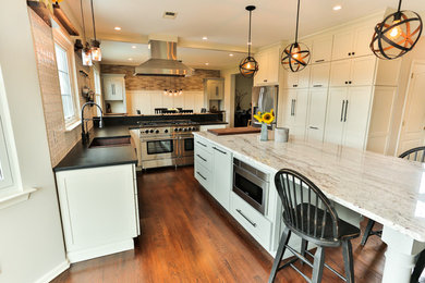 Eat-in kitchen - large farmhouse u-shaped medium tone wood floor and brown floor eat-in kitchen idea in New York with a farmhouse sink, recessed-panel cabinets, white cabinets, granite countertops, white backsplash, ceramic backsplash, stainless steel appliances, an island and white countertops