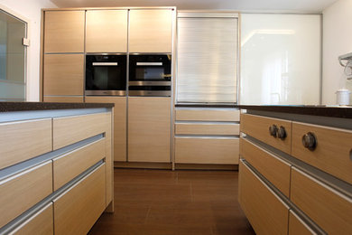 Große, Zweizeilige Moderne Wohnküche mit Unterbauwaschbecken, Küchenrückwand in Weiß, Kücheninsel, braunem Boden, flächenbündigen Schrankfronten, hellen Holzschränken, Mineralwerkstoff-Arbeitsplatte, Glasrückwand, Küchengeräten aus Edelstahl, dunklem Holzboden und brauner Arbeitsplatte in Nürnberg