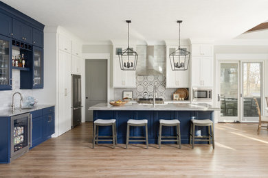 Eat-in kitchen - mid-sized transitional galley medium tone wood floor eat-in kitchen idea in Indianapolis with an undermount sink, glass-front cabinets, blue cabinets, granite countertops, white backsplash, granite backsplash, stainless steel appliances and an island