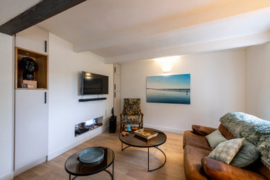 На фото: открытая гостиная комната среднего размера в стиле неоклассика (современная классика) с с книжными шкафами и полками, белыми стенами, светлым паркетным полом, телевизором на стене и балками на потолке
