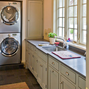 Photo of a medium sized traditional l-shaped utility room in Chicago with beaded cabinets, grey cabinets, soapstone worktops, beige walls, slate flooring, a stacked washer and dryer and a submerged sink.