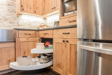 Eat-in kitchen - mid-sized traditional l-shaped dark wood floor eat-in kitchen idea in Denver with a farmhouse sink, shaker cabinets, light wood cabinets, quartz countertops, beige backsplash, stone tile backsplash, stainless steel appliances and an island
