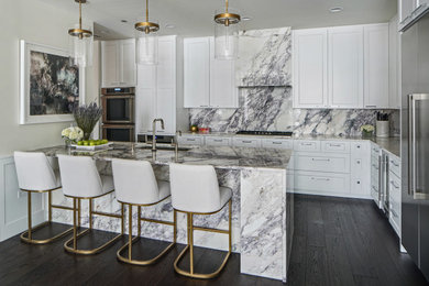 Photo of a large transitional l-shaped open plan kitchen in Chicago with an undermount sink, shaker cabinets, white cabinets, marble benchtops, beige splashback, marble splashback, stainless steel appliances, dark hardwood floors, with island, brown floor and beige benchtop.