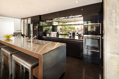 Design ideas for a contemporary single-wall open plan kitchen in Perth with an integrated sink, flat-panel cabinets, brown cabinets, stainless steel benchtops, mirror splashback, stainless steel appliances, dark hardwood floors and with island.