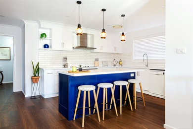 This is an example of a mid-sized modern l-shaped eat-in kitchen in Other with a double-bowl sink, flat-panel cabinets, white cabinets, solid surface benchtops, white splashback, ceramic splashback, white appliances, dark hardwood floors, with island, brown floor and white benchtop.