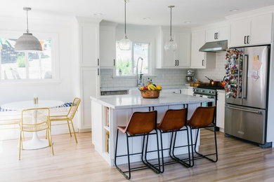 Inspiration for a mid-sized contemporary l-shaped brown floor kitchen remodel in Other with a farmhouse sink, shaker cabinets, white cabinets, white backsplash, subway tile backsplash, stainless steel appliances and an island