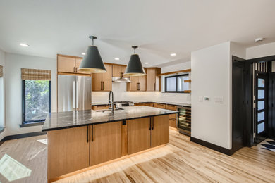 Kitchen - mid-sized modern light wood floor and brown floor kitchen idea in Denver with a farmhouse sink, flat-panel cabinets, brown cabinets, quartz countertops, white backsplash, porcelain backsplash, stainless steel appliances and black countertops
