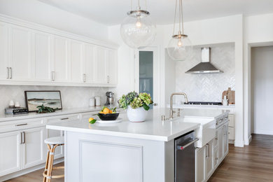 Inspiration for a mid-sized transitional u-shaped light wood floor and beige floor kitchen pantry remodel in Sacramento with a farmhouse sink, recessed-panel cabinets, white cabinets, quartz countertops, white backsplash, ceramic backsplash, stainless steel appliances, an island and white countertops