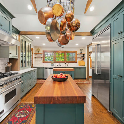 Example of a large classic u-shaped medium tone wood floor and exposed beam enclosed kitchen design in Providence with a farmhouse sink, shaker cabinets, green cabinets, white backsplash, subway tile backsplash, stainless steel appliances, two islands and white countertops