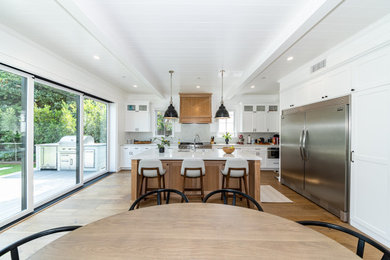 Photo of a large modern l-shaped kitchen/diner in Los Angeles with a submerged sink, shaker cabinets, white cabinets, marble worktops, white splashback, marble splashback, stainless steel appliances, medium hardwood flooring, an island, brown floors, white worktops and a wood ceiling.