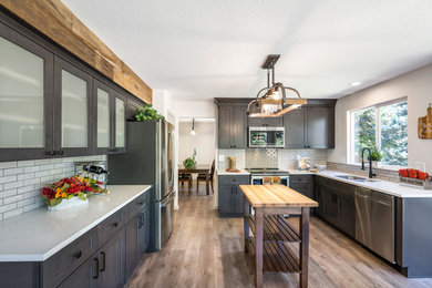 Large transitional u-shaped laminate floor and brown floor eat-in kitchen photo with an undermount sink, shaker cabinets, dark wood cabinets, granite countertops, gray backsplash, ceramic backsplash, stainless steel appliances, no island and white countertops
