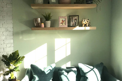 Small danish built-in desk medium tone wood floor study room photo in Surrey with green walls, a corner fireplace and a brick fireplace