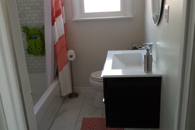 Small minimalist stone tile marble floor drop-in bathtub photo in Toronto with a wall-mount sink, flat-panel cabinets, dark wood cabinets, solid surface countertops, a two-piece toilet and beige walls