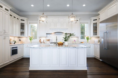 Photo of a large traditional u-shaped kitchen in New York with an undermount sink, raised-panel cabinets, white cabinets, marble benchtops, white splashback, subway tile splashback, stainless steel appliances, dark hardwood floors, with island, brown floor and white benchtop.