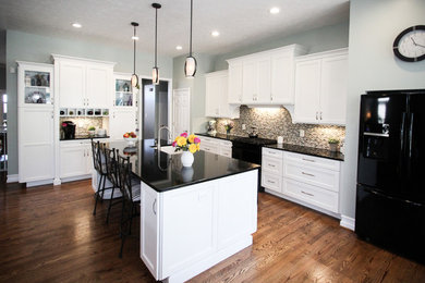 This is an example of a mid-sized transitional l-shaped eat-in kitchen in Columbus with a single-bowl sink, shaker cabinets, white cabinets, granite benchtops, metallic splashback, glass tile splashback, black appliances, light hardwood floors and with island.