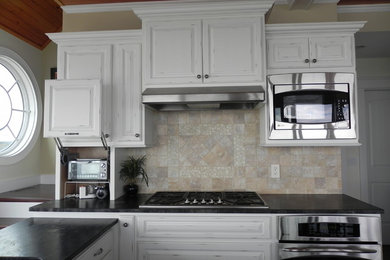 Example of a beach style l-shaped dark wood floor kitchen design in Providence with an undermount sink, stainless steel appliances, raised-panel cabinets, white cabinets, beige backsplash and no island