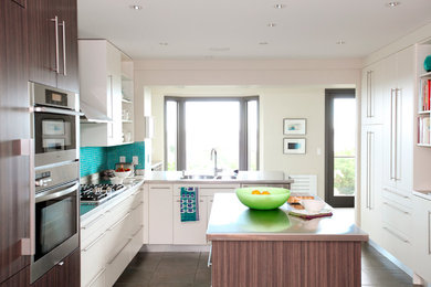 Inspiration for a mid-sized modern concrete floor enclosed kitchen remodel in Other with an undermount sink, flat-panel cabinets, medium tone wood cabinets, stainless steel countertops, blue backsplash, glass tile backsplash, paneled appliances and an island