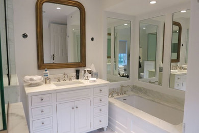 This is an example of a large transitional master bathroom in Chicago with furniture-like cabinets, white cabinets, an alcove tub, a corner shower, a two-piece toilet, white walls, marble floors, an undermount sink, marble benchtops, white floor, a hinged shower door and white benchtops.