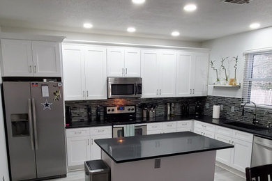 Inspiration for a contemporary l-shaped vinyl floor and gray floor eat-in kitchen remodel in Dallas with a single-bowl sink, shaker cabinets, white cabinets, quartzite countertops, black backsplash, glass tile backsplash, stainless steel appliances, an island and black countertops