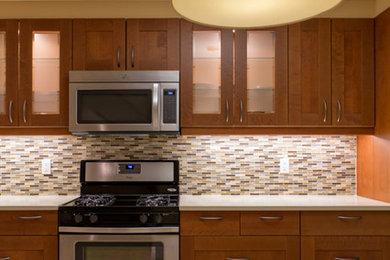 Example of a large transitional l-shaped porcelain tile kitchen design in New York with shaker cabinets, brown cabinets, quartz countertops, beige backsplash and stainless steel appliances