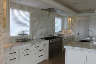 Example of a large light wood floor kitchen design in Hawaii with yellow cabinets, marble countertops, stainless steel appliances, an island, an undermount sink and white backsplash