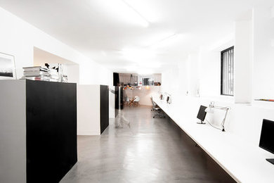 This is an example of a large modern home studio in Madrid with white walls, concrete flooring, a built-in desk and grey floors.