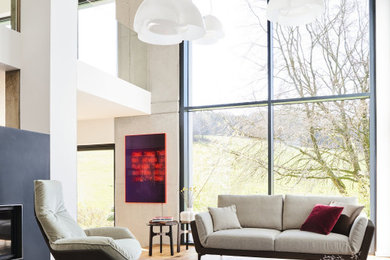 Großes, Fernseherloses, Offenes Modernes Wohnzimmer mit weißer Wandfarbe, hellem Holzboden, Kaminofen, verputzter Kaminumrandung und beigem Boden in Sonstige