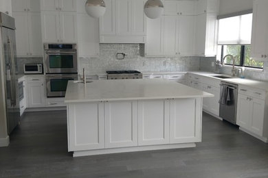 Inspiration for a large transitional u-shaped dark wood floor and gray floor enclosed kitchen remodel in Miami with an undermount sink, shaker cabinets, white cabinets, quartz countertops, white backsplash, stainless steel appliances, an island and white countertops