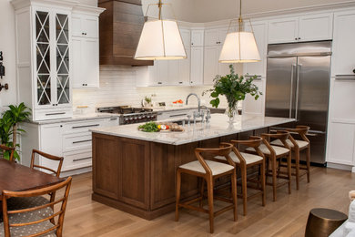 Kitchen - transitional l-shaped medium tone wood floor and brown floor kitchen idea in New York with an undermount sink, shaker cabinets, white cabinets, white backsplash, subway tile backsplash, stainless steel appliances, an island and gray countertops