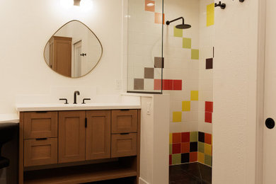 Large midcentury master bathroom in Denver with furniture-like cabinets, brown cabinets, a curbless shower, a one-piece toilet, multi-coloured tile, porcelain tile, white walls, porcelain floors, an undermount sink, engineered quartz benchtops, black floor, an open shower, white benchtops, a shower seat, a double vanity, a freestanding vanity and vaulted.
